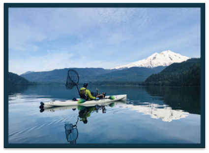 A fisher on a Kyak on Baker Lake Sockeye Fishing - mountain covered in snow in the background and reflecting onto the calm lake water.